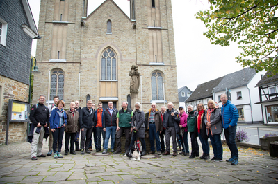 Gruppenfoto von einer Wandergruppe mit Wanderbahnhof-Aktionspate Manuel Andrack vor einer historischen Kirche. Vor der Menschengruppe sitzt ein Hund.