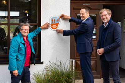 Die Verleihung der begehrten Wanderbahnhof-​Plakette in Sondern. v. l. n. r.: Manuel Andrack (Wanderexperte), Peter Weber (Bürgermeister Olpe), Dr. Dirk Günnewig (Verkehrsministerium NRW).
