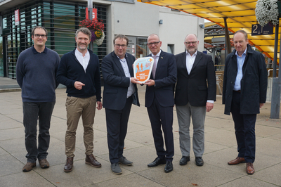 v.l.n.r.: Mathias von Kutzleben (Kompetenzcenter Marketing NRW), Lukas Furth (Geschäftsführer Verkehrsverein Emsdetten), Oliver Krischer (Minister für Umwelt, Naturschutz und Verkehr des Landes Nordrhein-​Westfalen), Oliver Kellner (Bürgermeister Emsdetten), Helmuth Schäckel (Gebäudemanagement Bahnhof Emsdetten), Michael Jansen (Deutsche Bahn, Leiter Bahnhofsmanagement Münster/Westf.) stehen mit der Wanderbahnhofsplakette vor dem Bahnhofsgebäude Emsdetten.