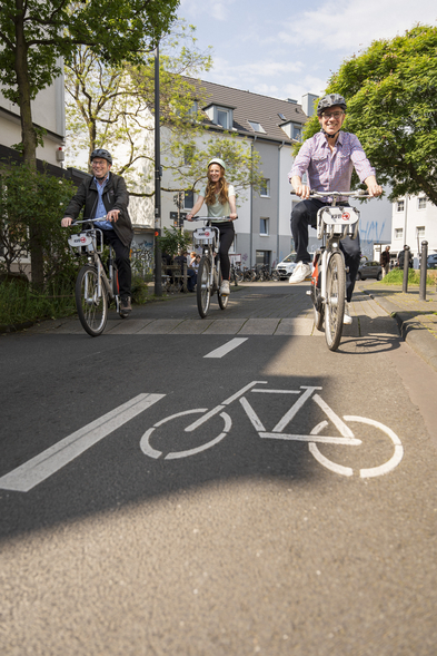 Minister Oliver Krischer, Rebecca Schirge und Dr. Norbert Reinkober fahren auf Leihrädern über eine sonnige Straße.