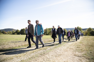 Wander-Bf_2018_Galerie_10_Foto-Emanuel_Bloedt.JPG Verkehrsminister Hendrik Wüst und Aktionspate Manuel Andrack mit anderen Teilnehmer*innen bei der Wanderung über einen Feldweg und unter blauem Himmel zum NRW-Wanderbahnhof 2018.