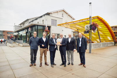 v.l.n.r.: Mathias von Kutzleben (Kompetenzcenter Marketing NRW), Lukas Furth (Geschäftsführer Verkehrsverein Emsdetten), Oliver Krischer (Minister für Umwelt, Naturschutz und Verkehr des Landes Nordrhein-​Westfalen), Oliver Kellner (Bürgermeister Emsdetten), Helmuth Schäckel (Gebäudemanagement Bahnhof Emsdetten), Michael Jansen (Deutsche Bahn, Leiter Bahnhofsmanagement Münster/Westf.) stehen mit der Wanderbahnhofsplakette vor dem Bahnhofsgebäude Emsdetten.