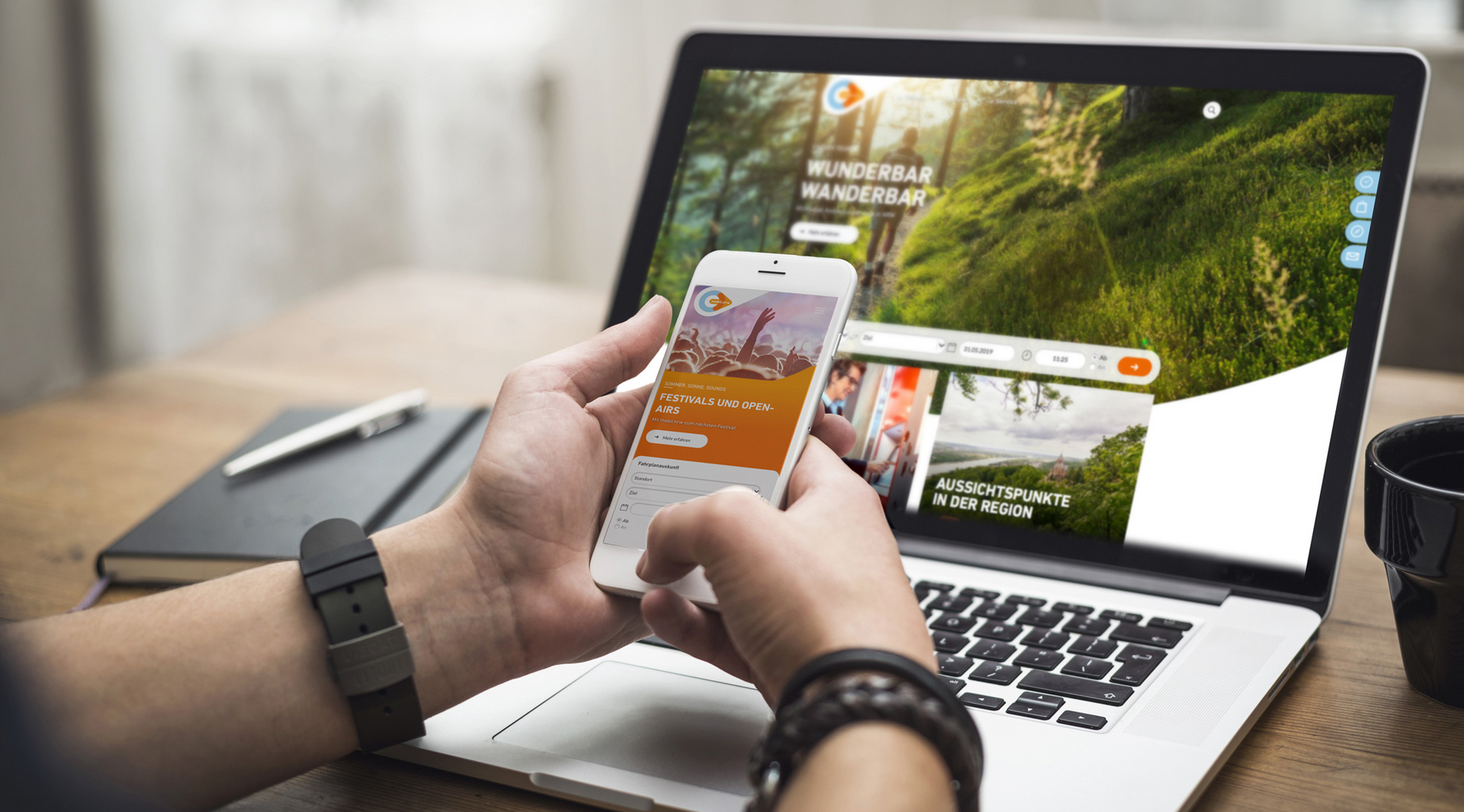 Zwei Hände halten ein weißes Smartphone vor einem Laptop. Auf dem Handy ist die mobil.nrw App zu sehen mit einer Aktion zur Festivalsaison. Auf dem Laptop Bildschirm ist die mobil.nrw Desktop Seite zu sehen mit einem Wander-Spezial.