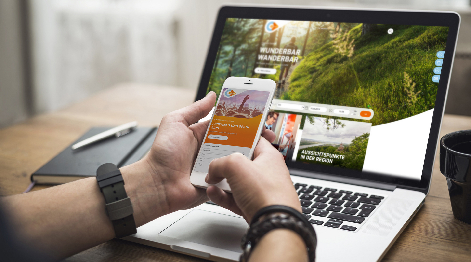 Zwei Hände halten ein weißes Smartphone vor einem Laptop. Auf dem Handy ist die mobil.nrw App zu sehen mit einer Aktion zur Festivalsaison. Auf dem Laptop Bildschirm ist die mobil.nrw Desktop Seite zu sehen mit einem Wander-Spezial.