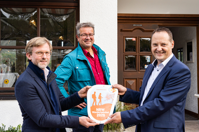 Die Verleihung der Wanderbahnhof-​Plakette in Sondern. v. l. n. r.: Dr. Dirk Günnewig (Verkehrsministerium NRW), Manuel Andrack (Wanderexperte), Peter Weber (Bürgermeister Olpe). 
