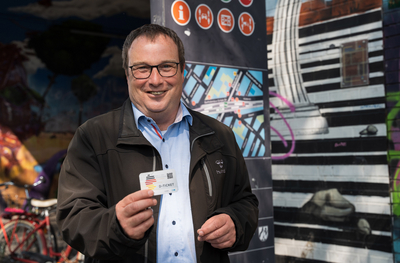 Minister Oliver Krischer hält vor der Stele einer Mobilstation das Deutschlandticket nach oben.