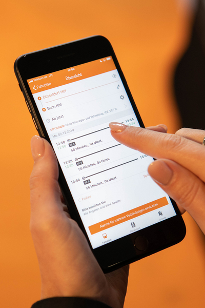 Nahaufnahme der mobil.nrw App auf einem Handybildschirm vor einem orangefarbenen Hintergrund.