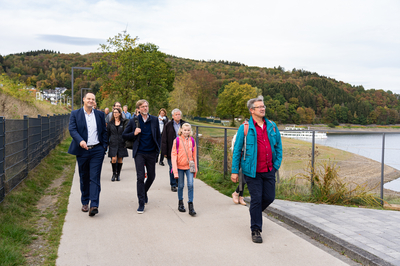 Eine große Menschengruppe wandert an einem herbstlichen See, unter anderem Peter Weber (Bürgermeister Olpe), Dr. Dirk Günnewig (Verkehrsministerium NRW) und Manuel Andrack (Wanderexperte),